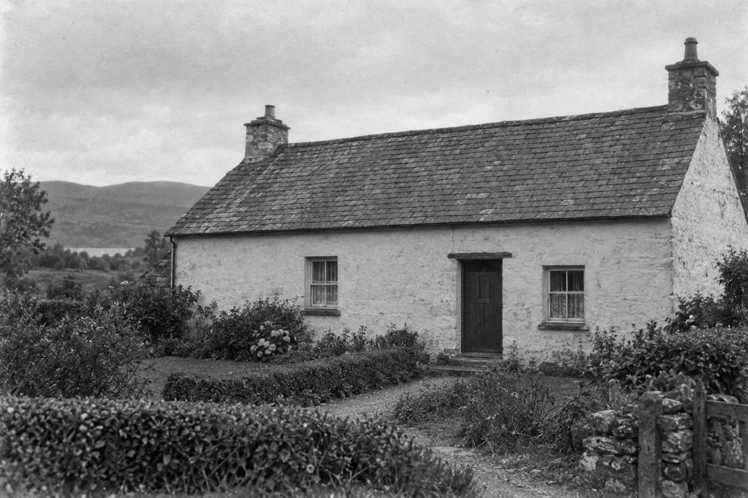 La scansione sbiadita e brunastra di un cottage prima e dopo il restauro in bianco e nero, con toni più profondi e i piccoli graffi e segni di polvere riparati