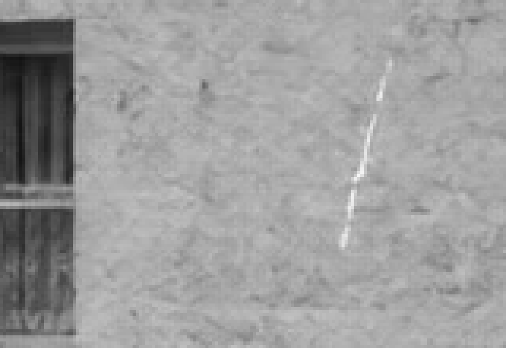 Il graffio bianco sull’intonaco a destra della finestra di sinistra, ingrandito, prima della riparazione
